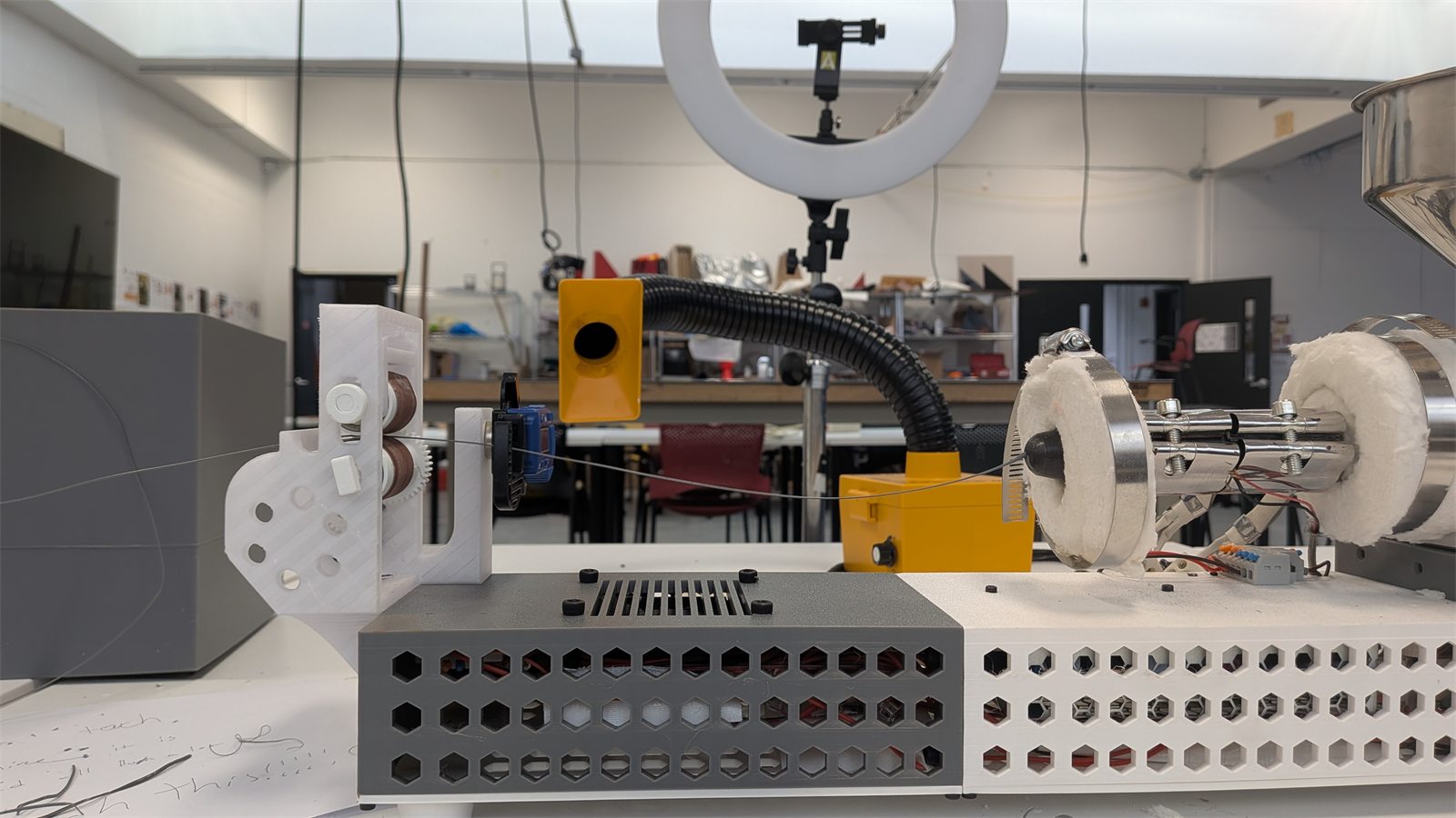 Extrusion setup on a workbench with a filament spool, motor, and bench hardware.
