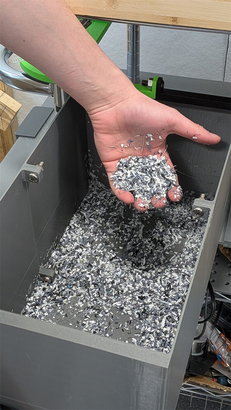 Hand holding shredded plastic flakes above a bin of processed material.